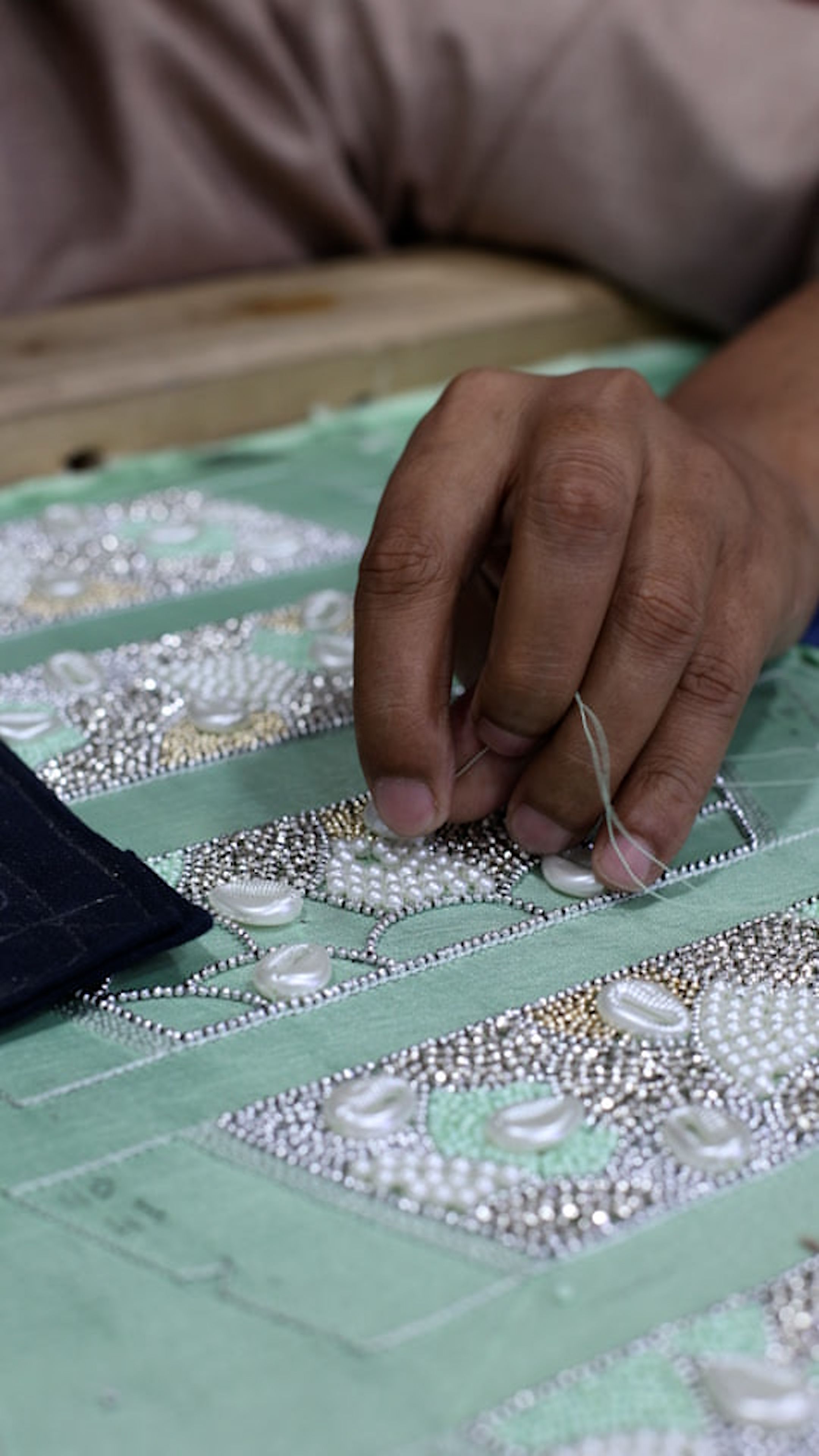 Close-up of artisan hand embroidering intricate designs on fabric in Lahore, Pakistan.