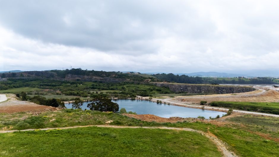 Vista aérea de un paisaje de cantera con exuberante vegetación y un cuerpo de agua sereno en Cantabria, España.