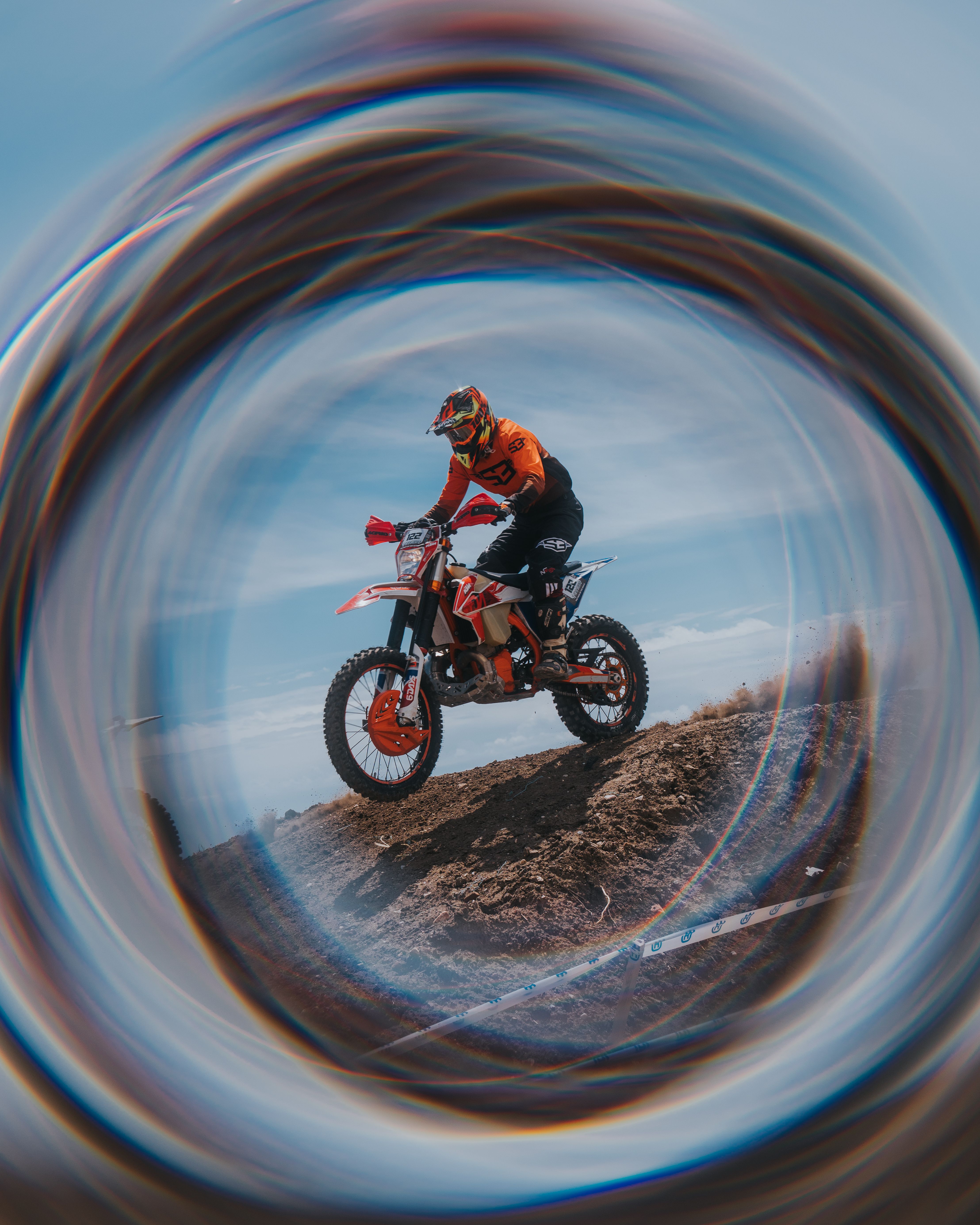Motocross racer performing a jump on dirt track, framed by circular lens effect.