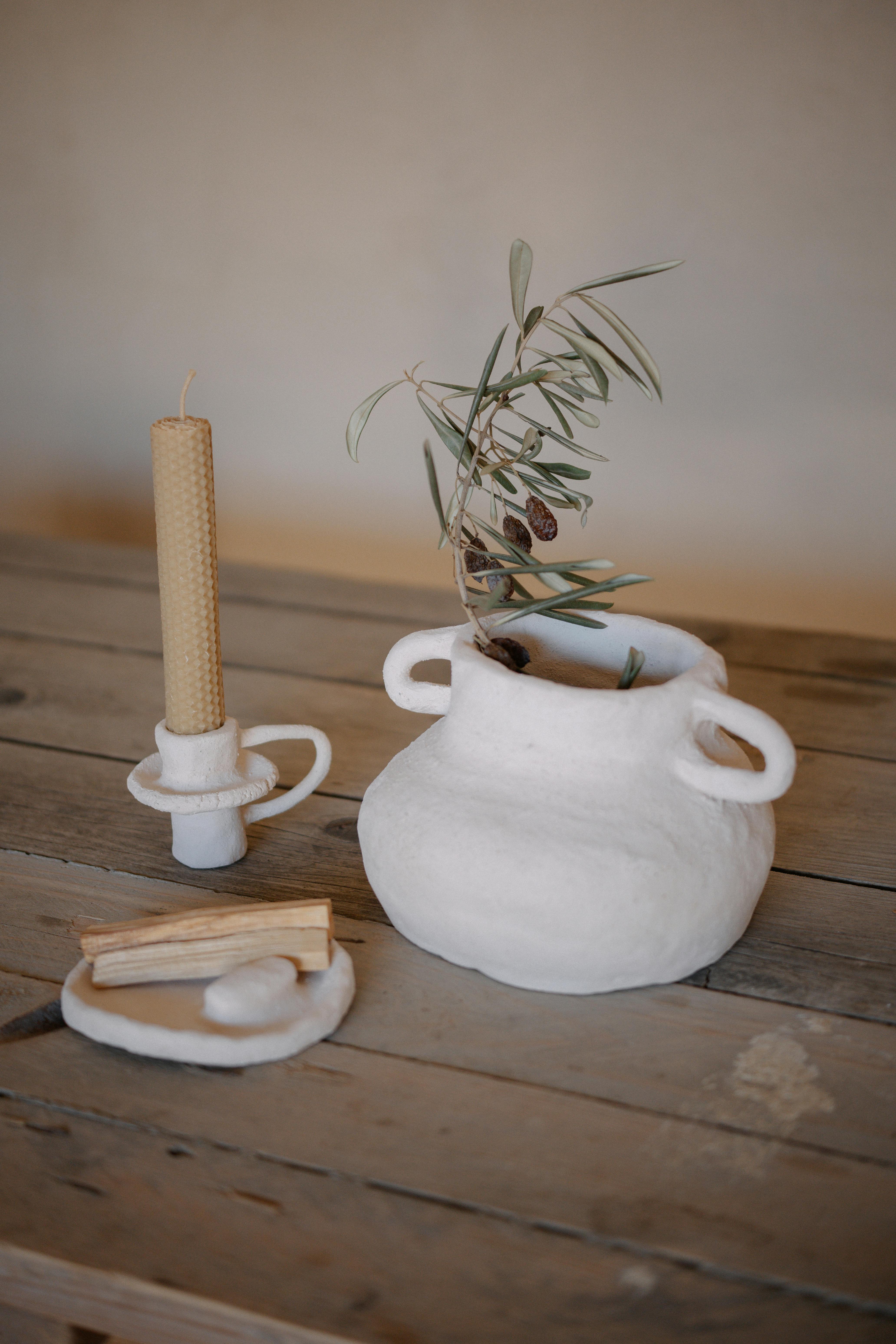 A minimalist wabi-sabi setup featuring a ceramic vase with olive branches and a candle on a rustic table.