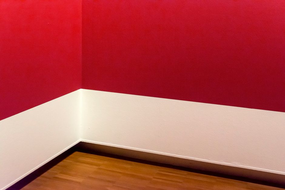 A minimalist room corner with striking red walls and wooden flooring, showcasing modern design.