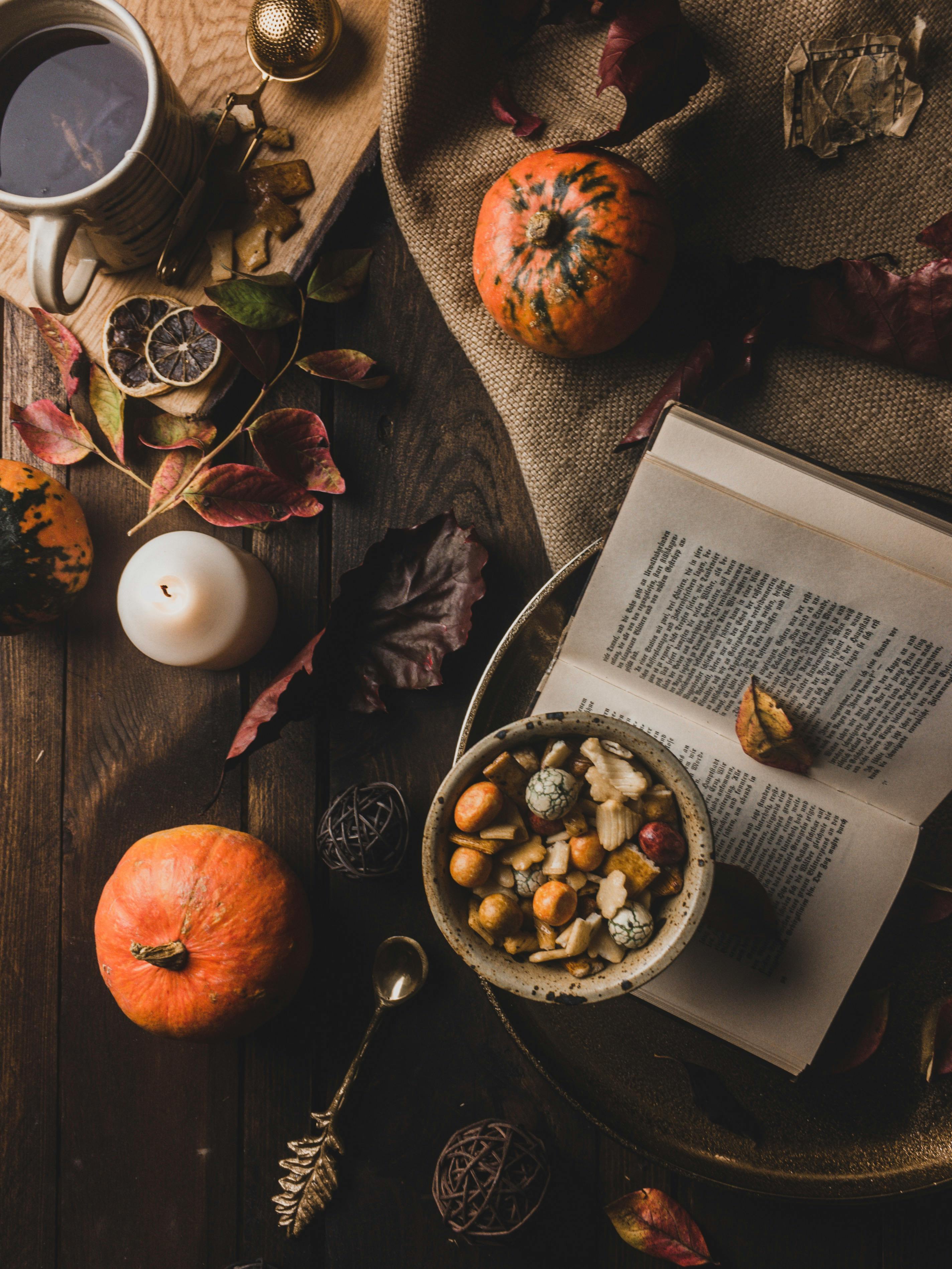 top view of a book and a cup of tea surrounded with an assortment of thing on top of a wooden table