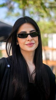 Fashionable woman with sunglasses smiling outdoors on a sunny day.