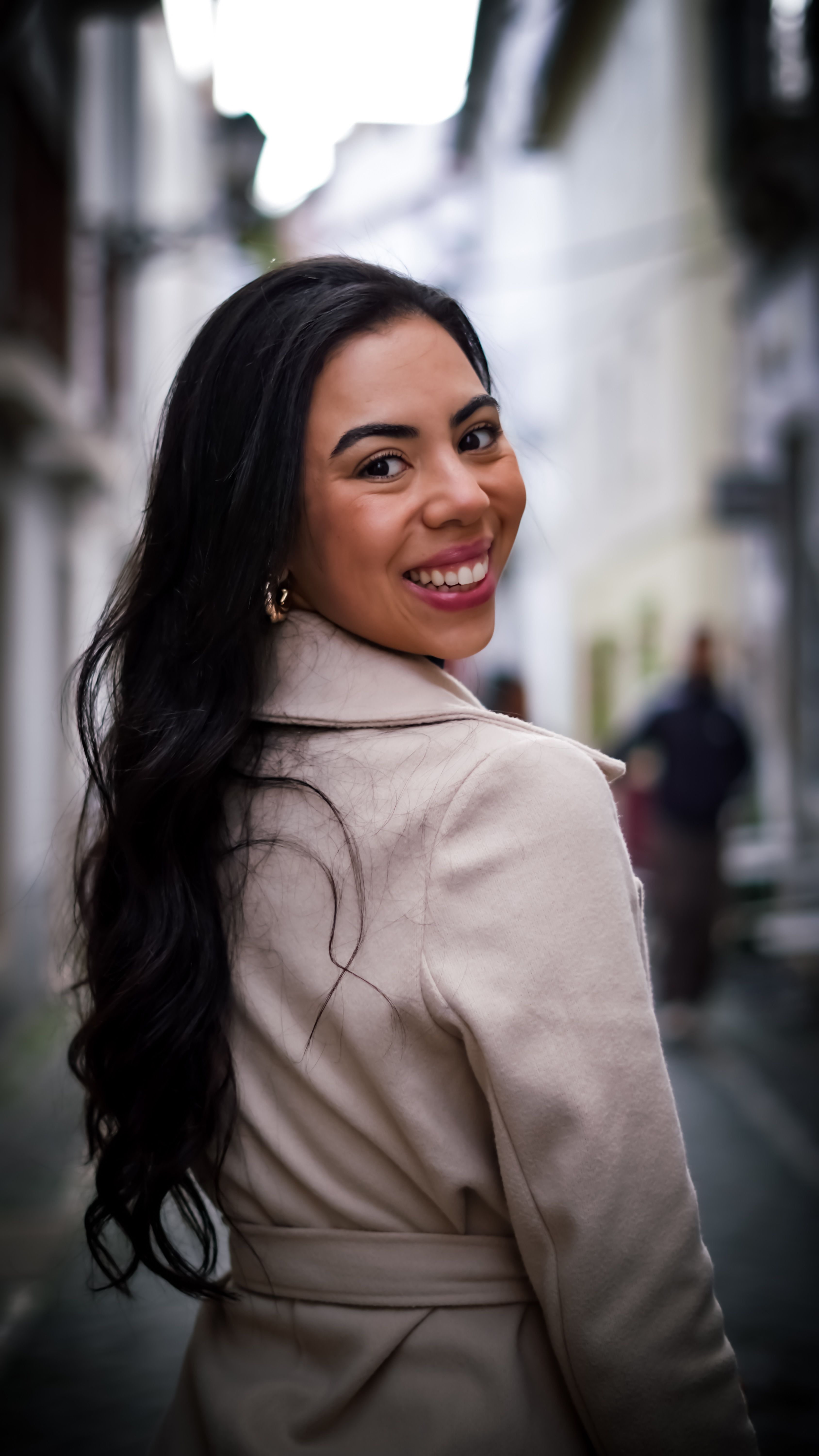 Cheerful woman wearing a stylish coat, smiling on a bustling city street.