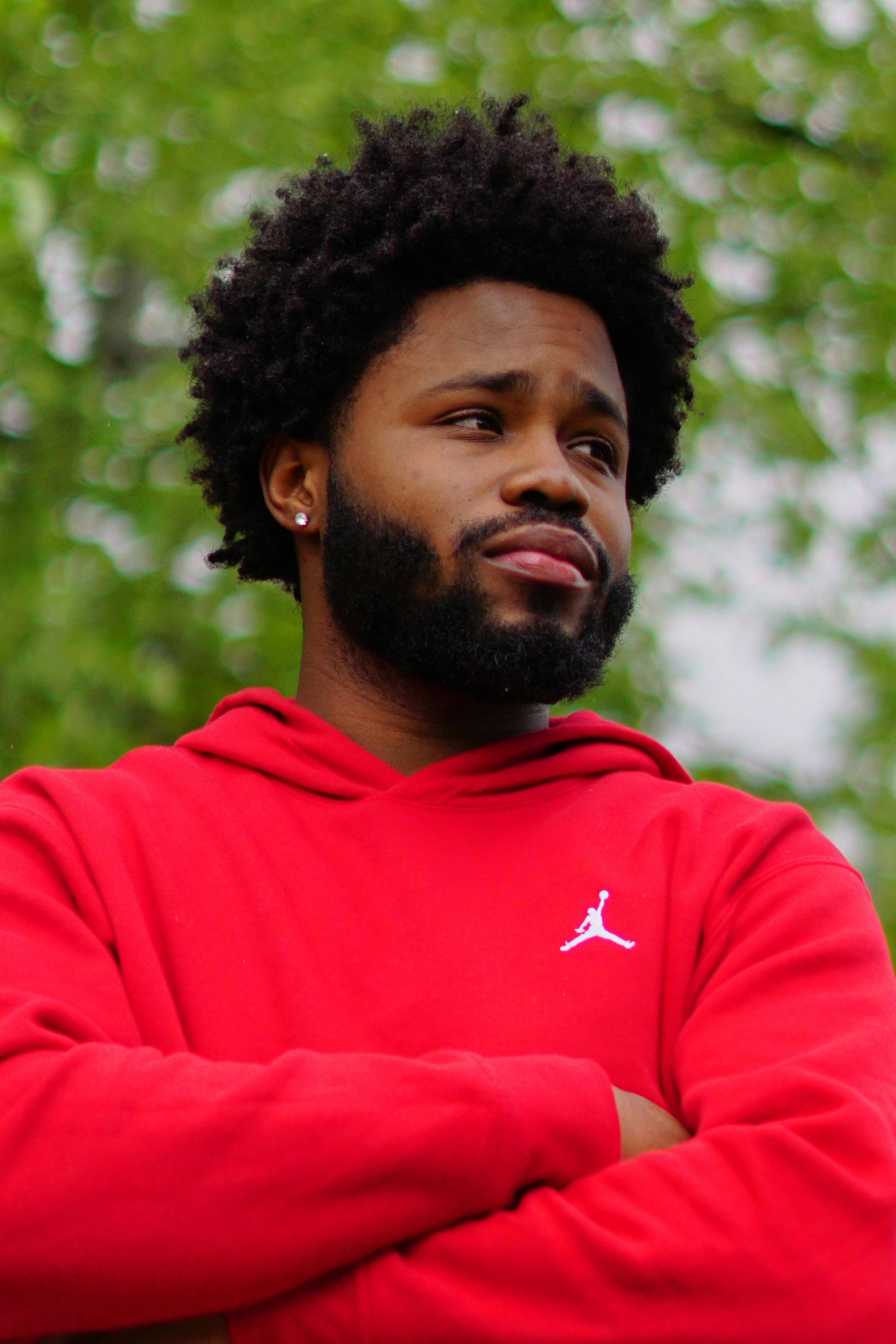 Portrait of a confident man wearing a red hoodie amidst lush green foliage.