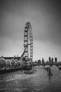 Black and white image of the London Eye overlooking River Thames with city skyline in the background.