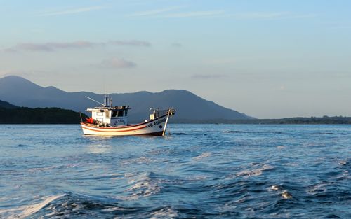 Free A fishing boat sails on a calm sea with mountains in the background. Stock Photo