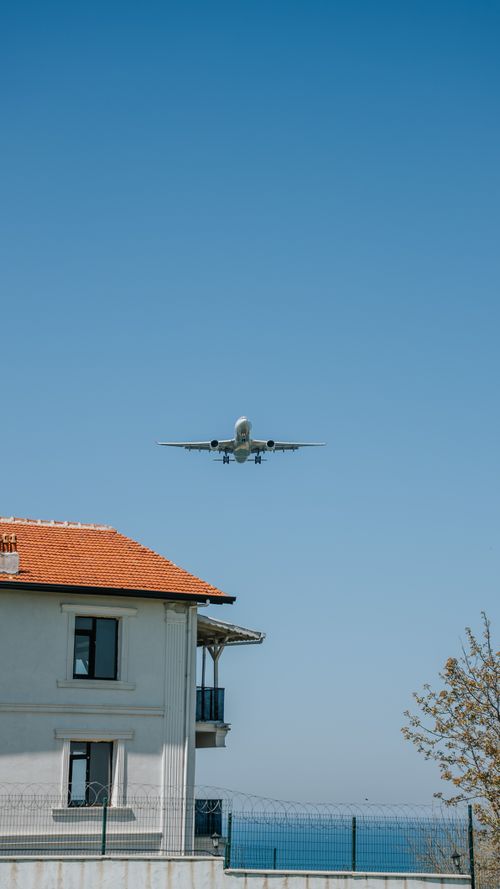 Free Airplane approaches over a house with a clear blue sky above, depicting urban aviation. Stock Photo