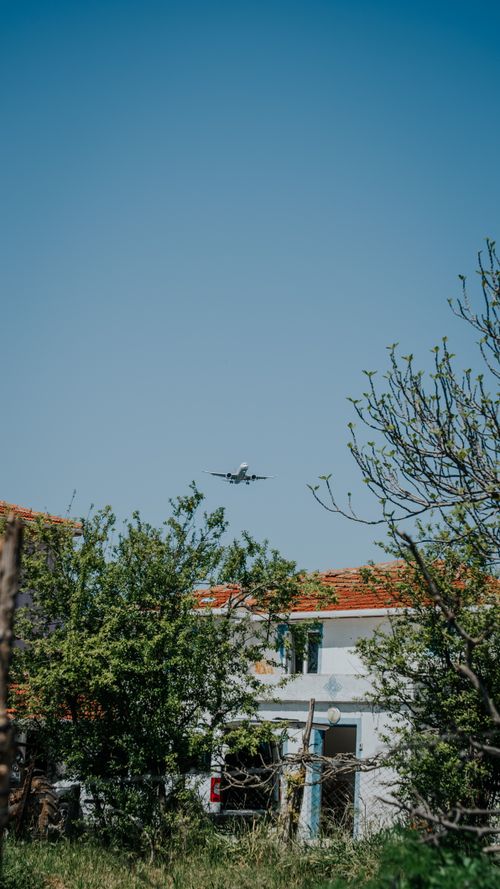 Free A scenic view of a plane flying over a countryside house with a clear sky. Stock Photo