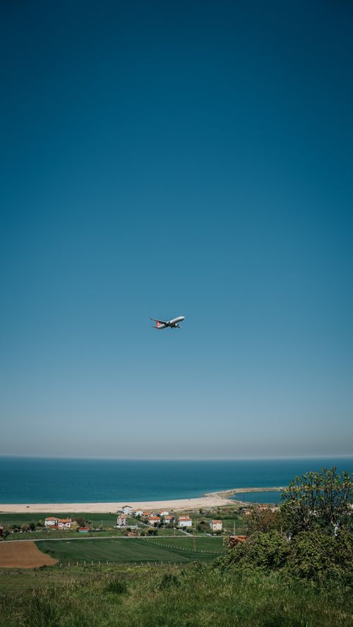 Free A scenic view of a plane flying over a vibrant coastal landscape with blue skies. Stock Photo