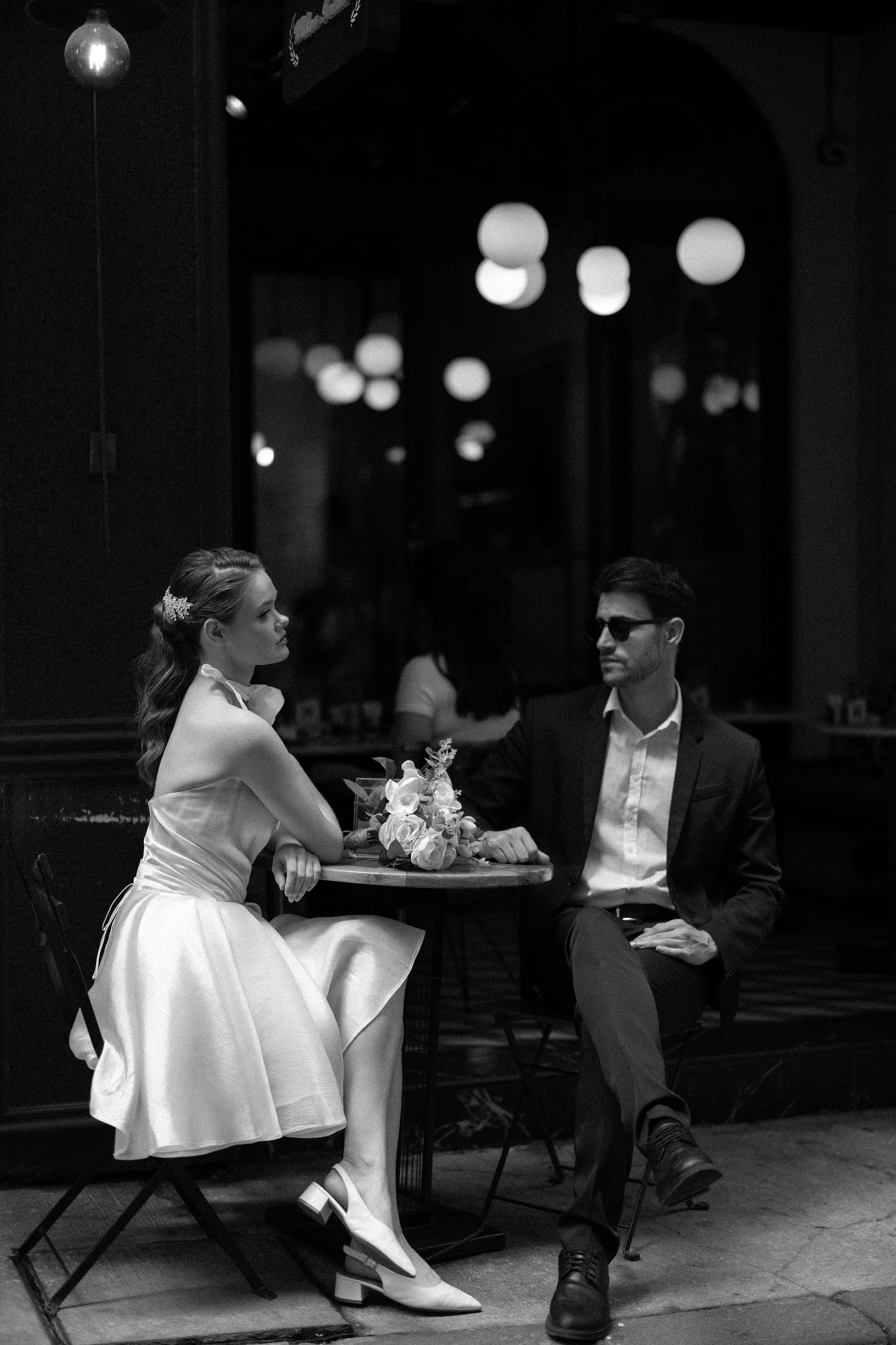 Stylish couple enjoying an outdoor cafe experience in a classic black and white photograph.