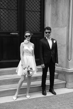 Stylish couple in sunglasses posing for a black and white wedding photo outside.
