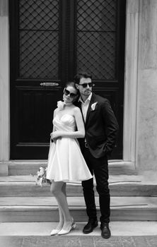A stylish couple poses in black and white attire against a classic doorway.