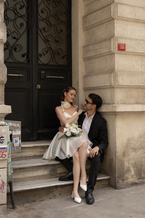 Free Elegant couple in wedding attire sitting on stairs by a vintage door capturing a romantic moment. Stock Photo