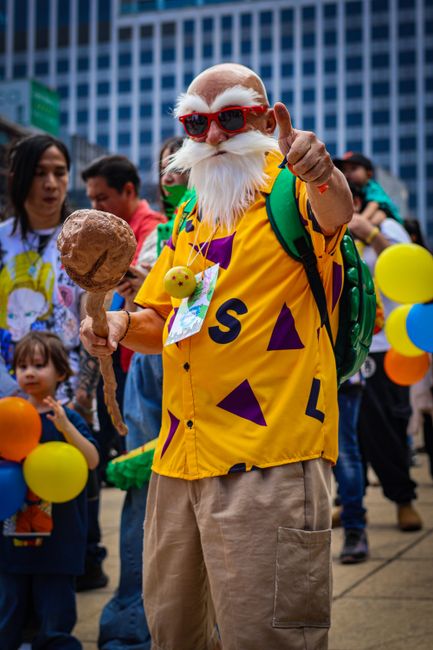 A vibrant cosplay enthusiast poses during a lively outdoor event, showcasing colorful attire and props.