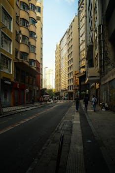 A city street lined with towering buildings and pedestrians walking along the sidewalk in daylight.