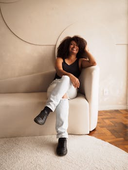 A cheery woman in casual attire relaxes on a modern sofa, exuding warmth and comfort.