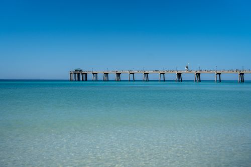 Free A beautiful ocean pier stretching over crystal clear turquoise waters beneath a bright blue sky. Stock Photo