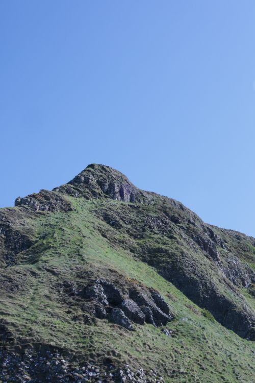 Free A green rocky hill set against a clear blue sky in Northern Ireland for a serene landscape view. Stock Photo