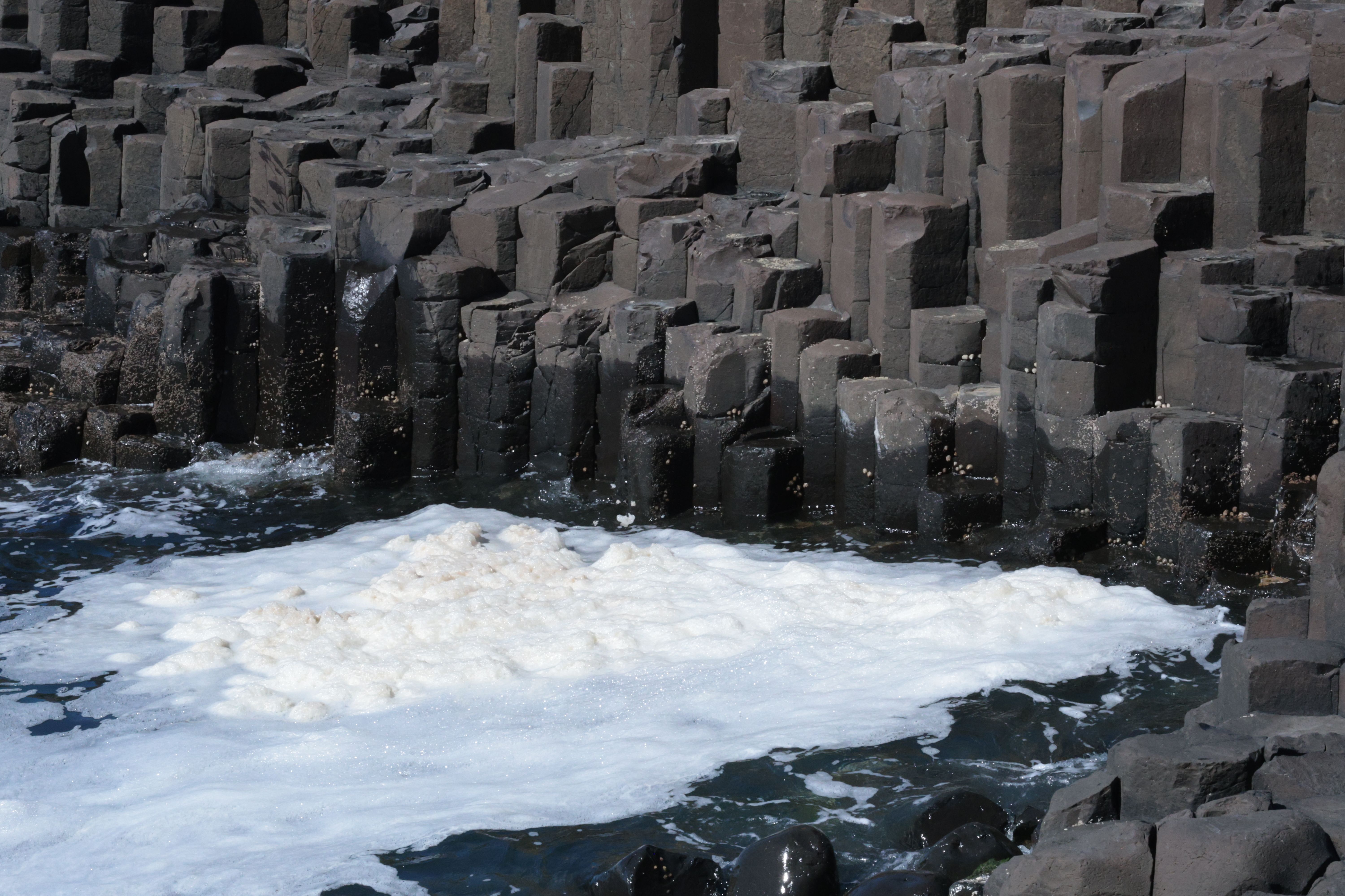 Natural hexagonal basalt columns at Giant's Causeway with sea foam.