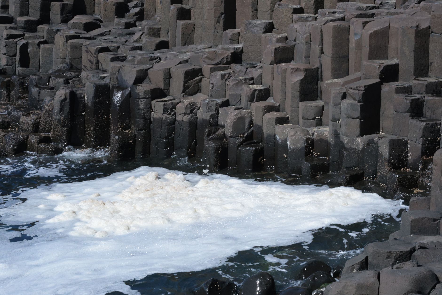 Natural hexagonal basalt columns at Giant's Causeway with sea foam.