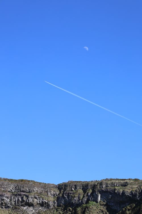 Free Stunning view of Northern Ireland cliffs under a bright blue sky with a contrail and moon visible. Stock Photo