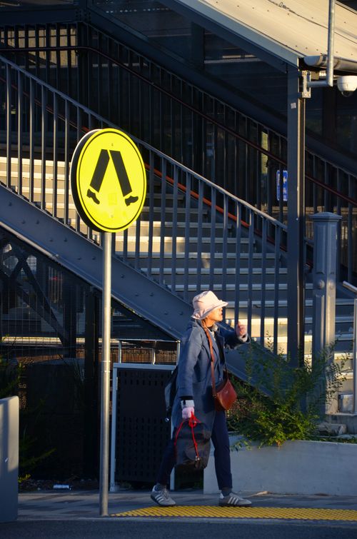 Free Elderly woman walking past a caution sign at a train station, during sunset. Stock Photo