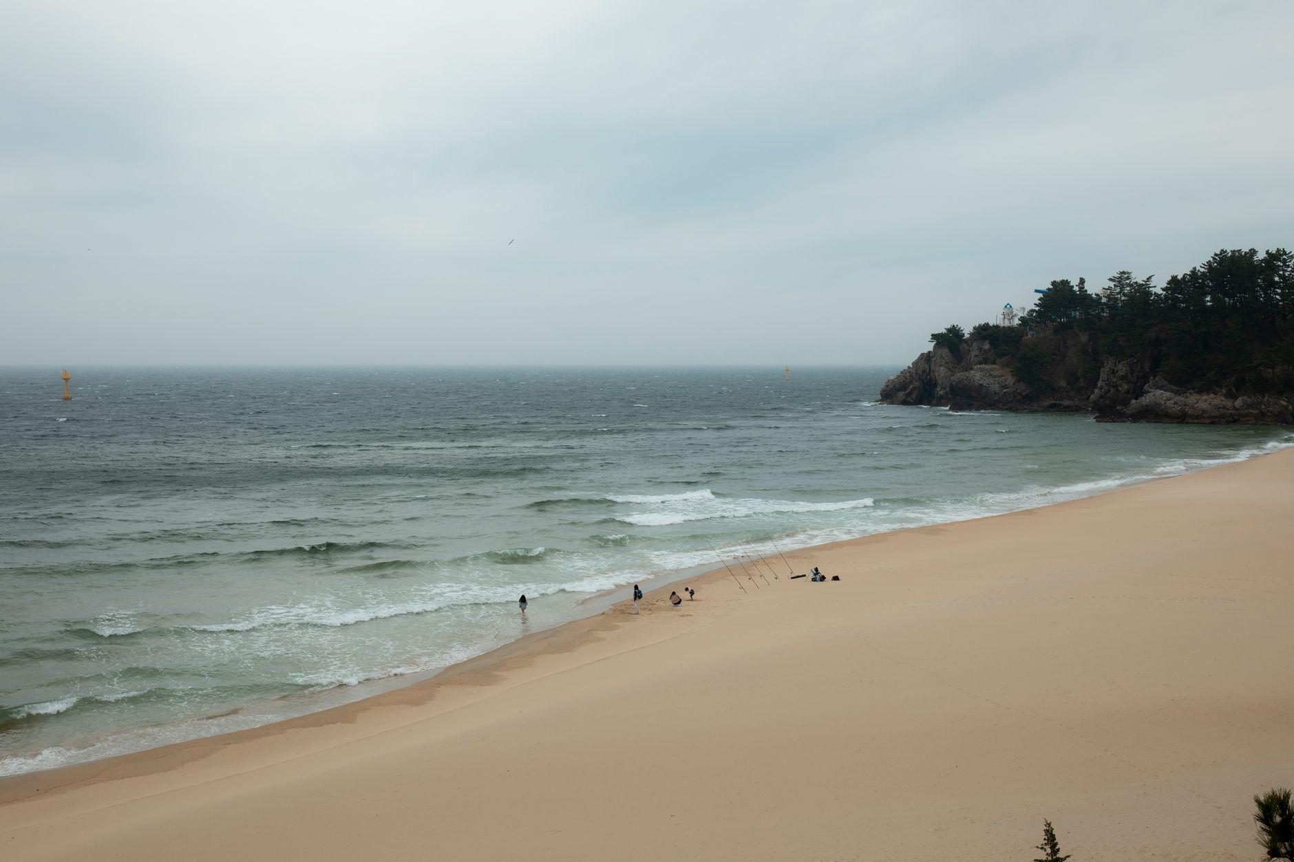 A serene beach scene with gentle waves and a distant rocky cliff under overcast skies.