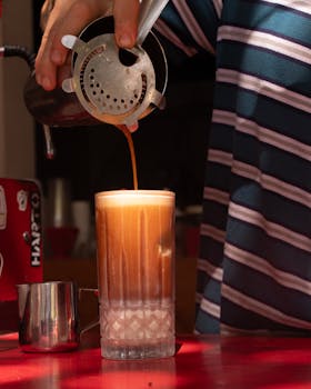 A barista skillfully pours cold brew coffee into a tall glass, creating a refreshing beverage.