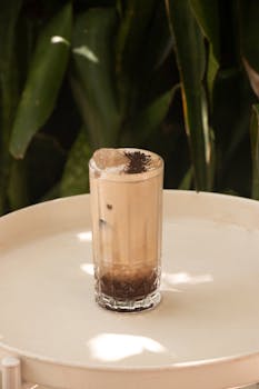 A tall glass of iced latte with coffee garnish on a bright outdoor table.