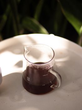 Stylish glass coffee carafe with freshly brewed coffee on a white surface in natural light.