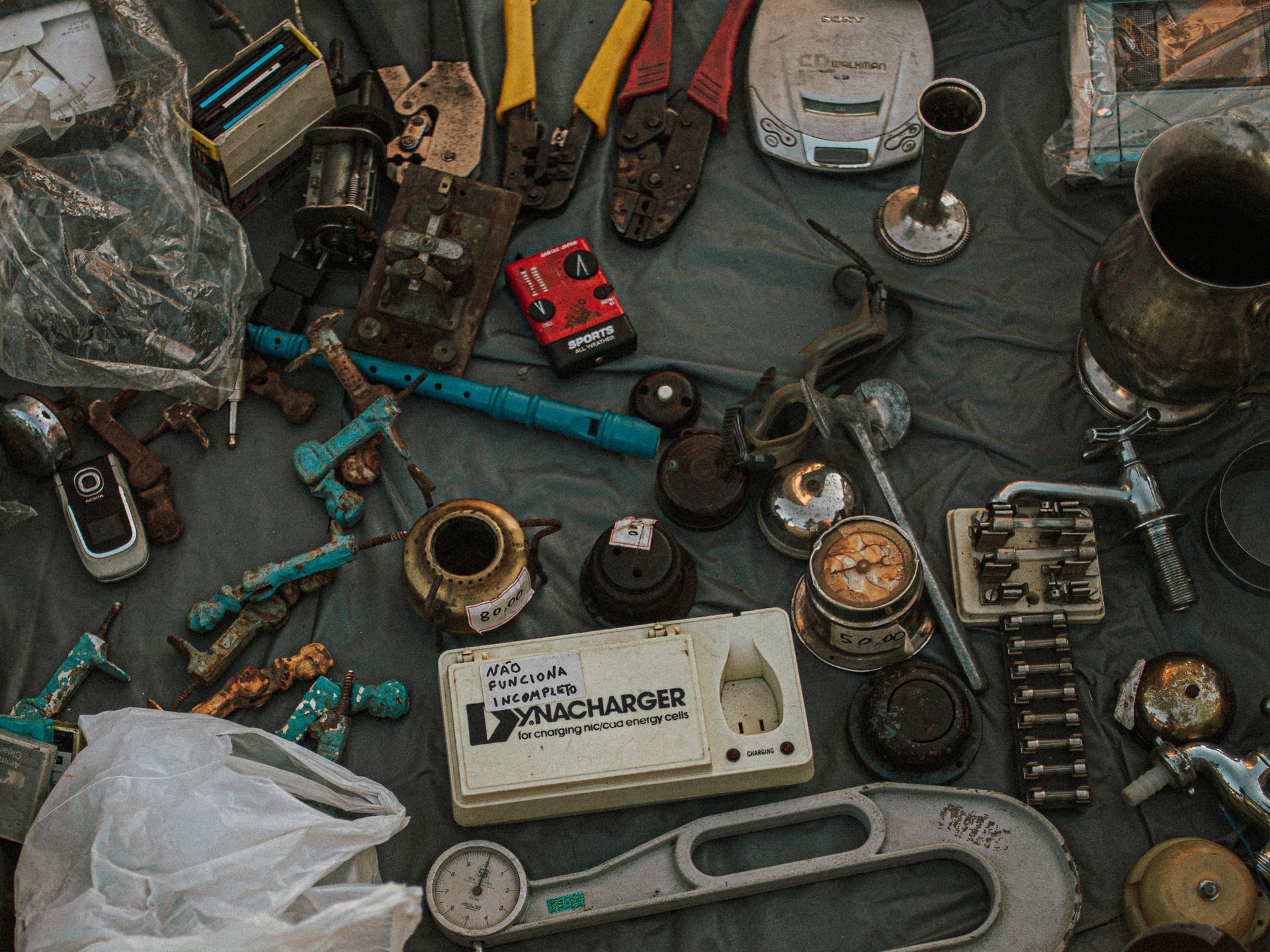 Scattered assortment of old metal tools, gadgets, and household items displayed at an outdoor flea market.