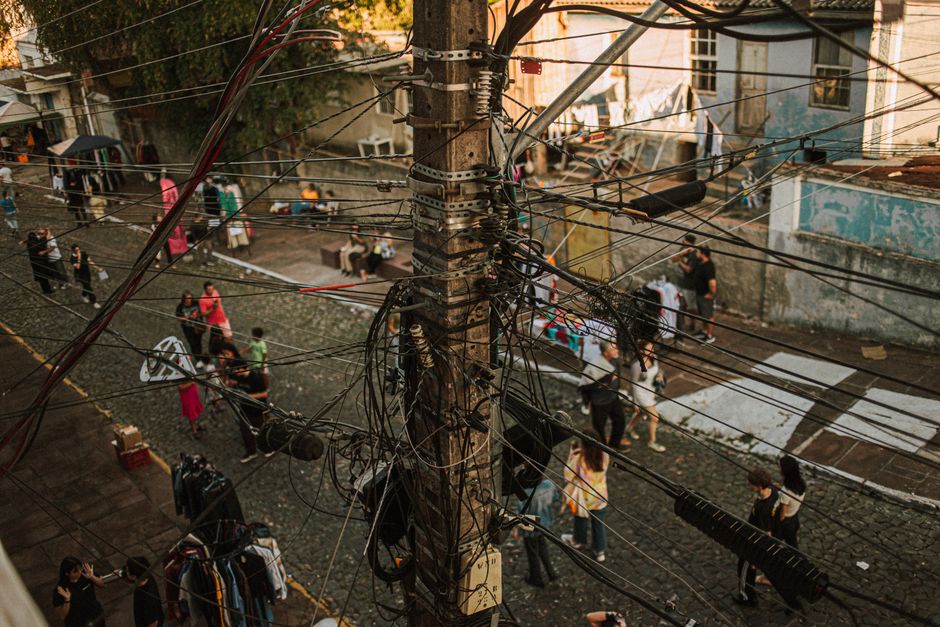 A busy urban street scene with tangled utility cables and people interacting below.