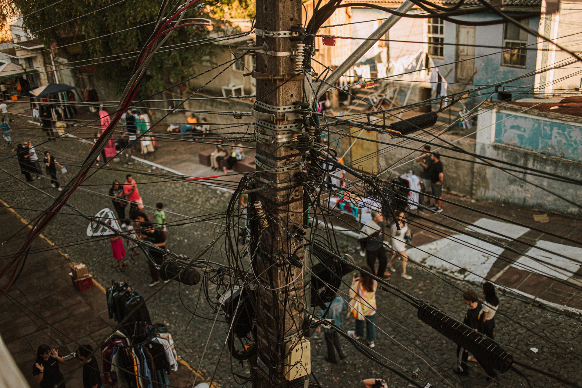 A busy urban street scene with tangled utility cables and people interacting below.