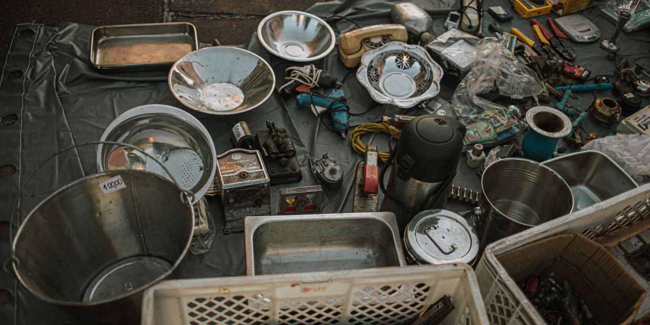 Assorted metal items and vintage tools displayed at an outdoor flea market on asphalt.