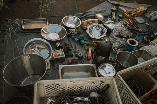 Free Assorted metal items and vintage tools displayed at an outdoor flea market on asphalt. Stock Photo