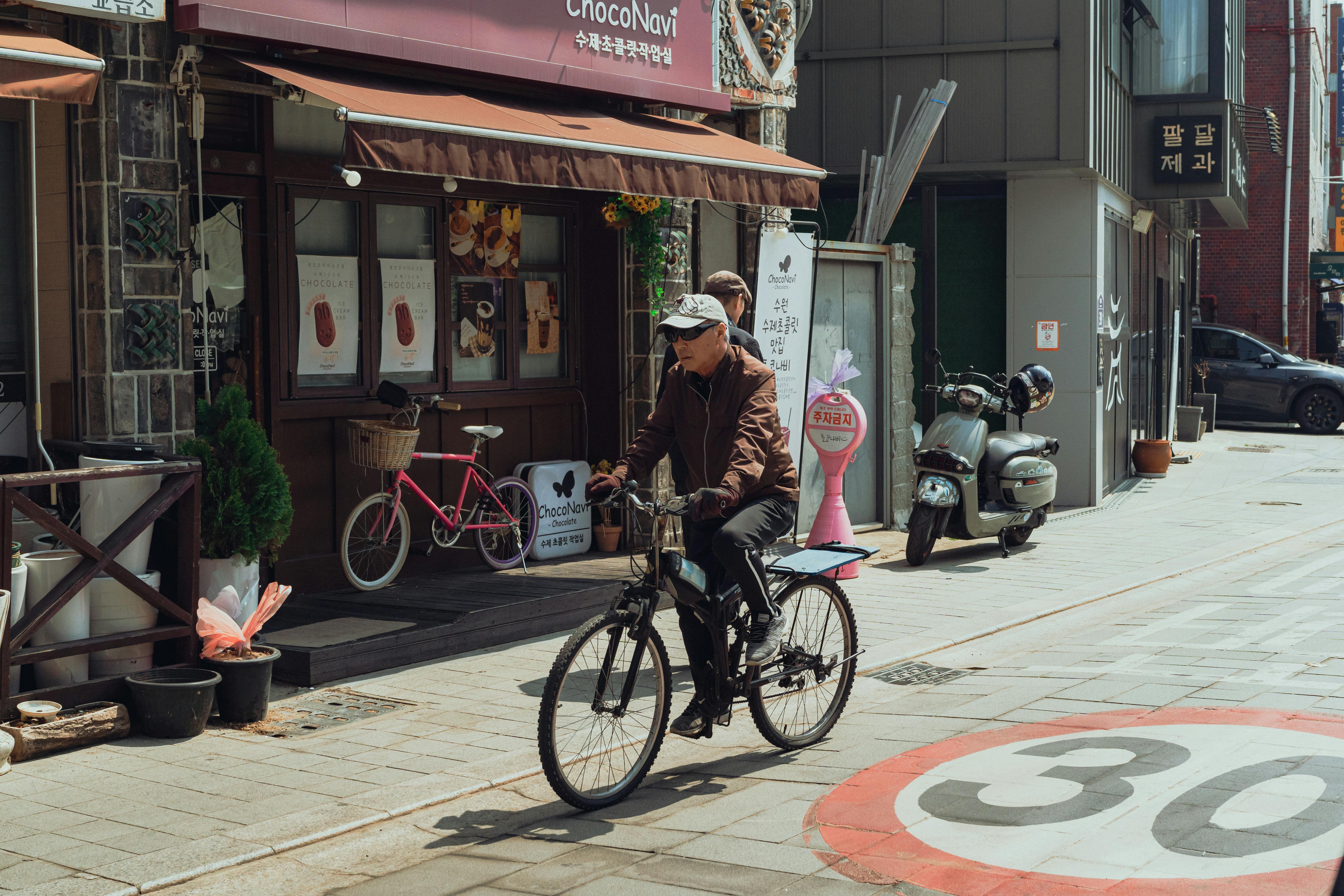 Street scene of an elderly man cycling past shops in Suwon-si, South Korea.