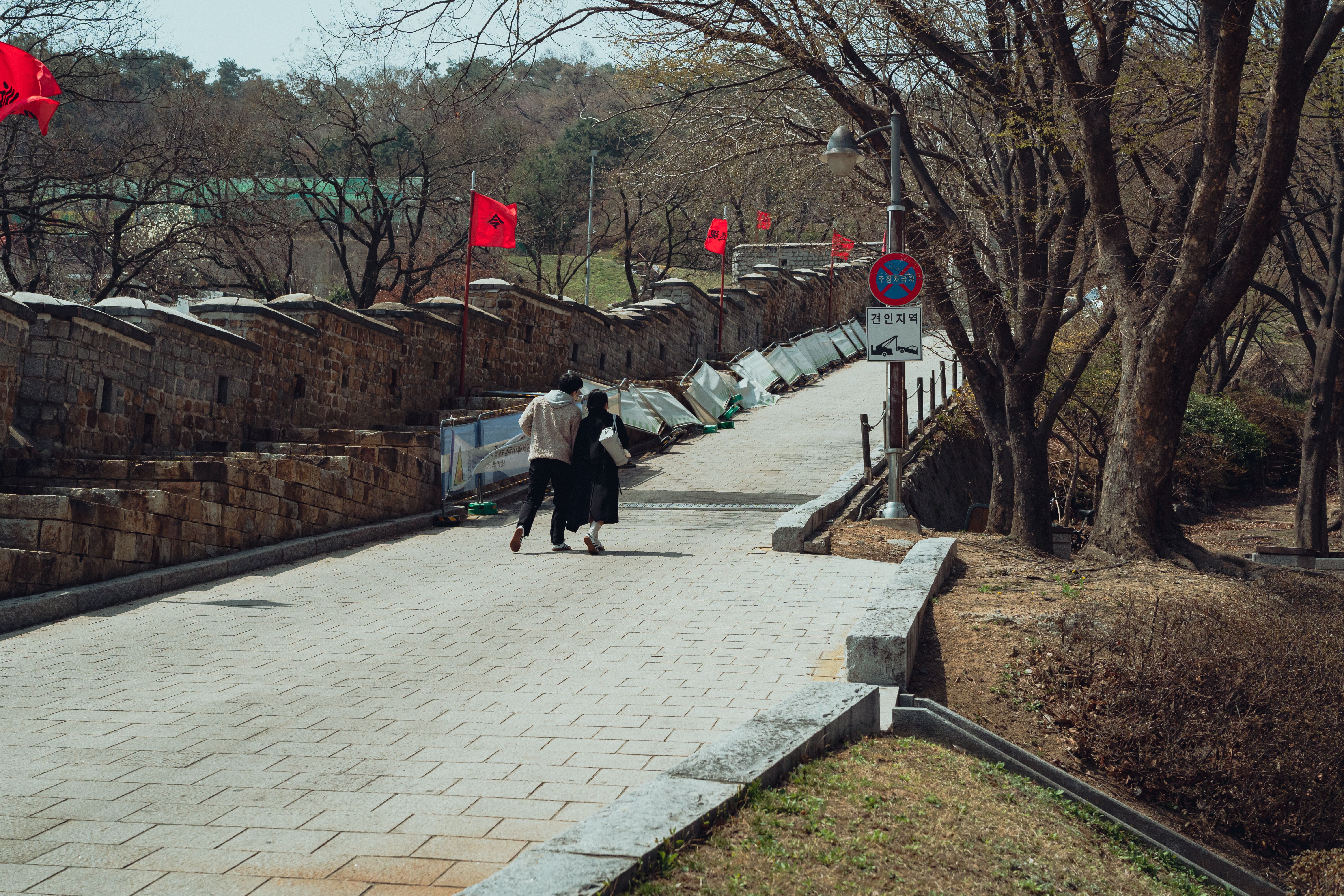 A couple walks along the historic Suwon Hwaseong Fortress path, adorned with red flags.