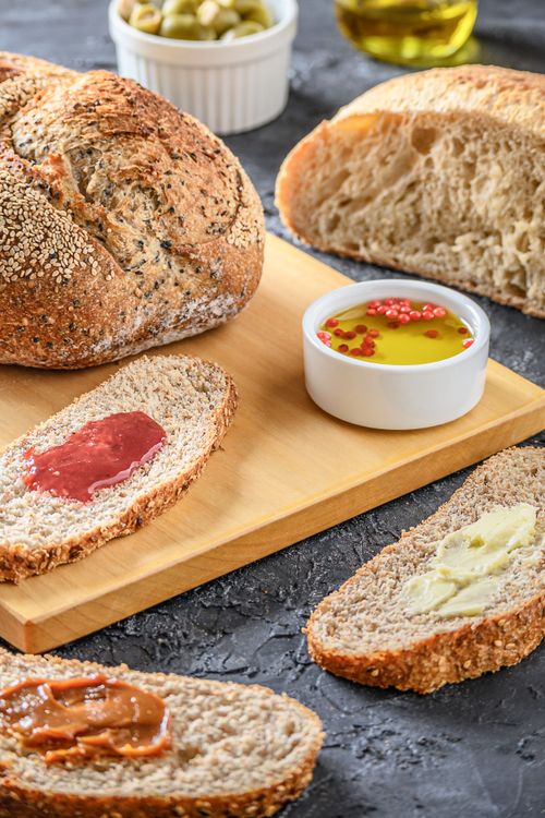 Free Fresh artisan bread with butter, jam, and olive oil on a wooden board, creating a rustic dining atmosphere. Stock Photo