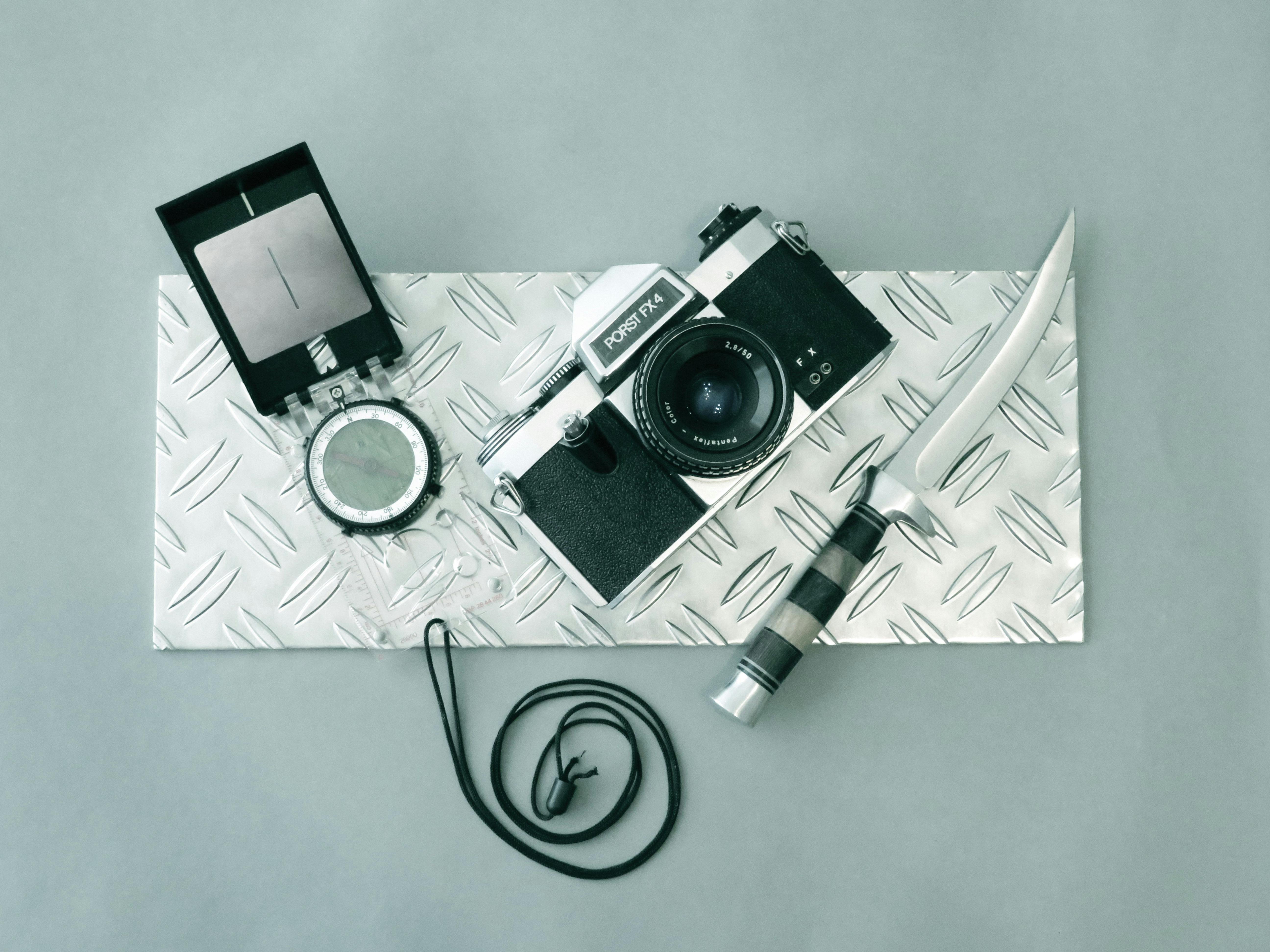 Gratis Una cámara vintage, una brújula y un cuchillo colocados sobre una placa de metal texturizada para lograr una estética resistente y clásica. Foto de stock