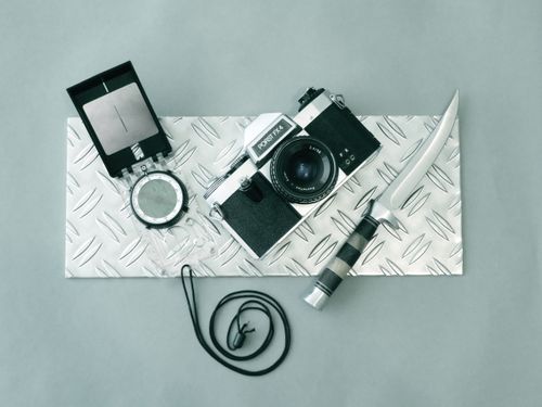 Free A vintage camera, compass, and knife placed on a textured metal plate for a rugged, classic aesthetic. Stock Photo