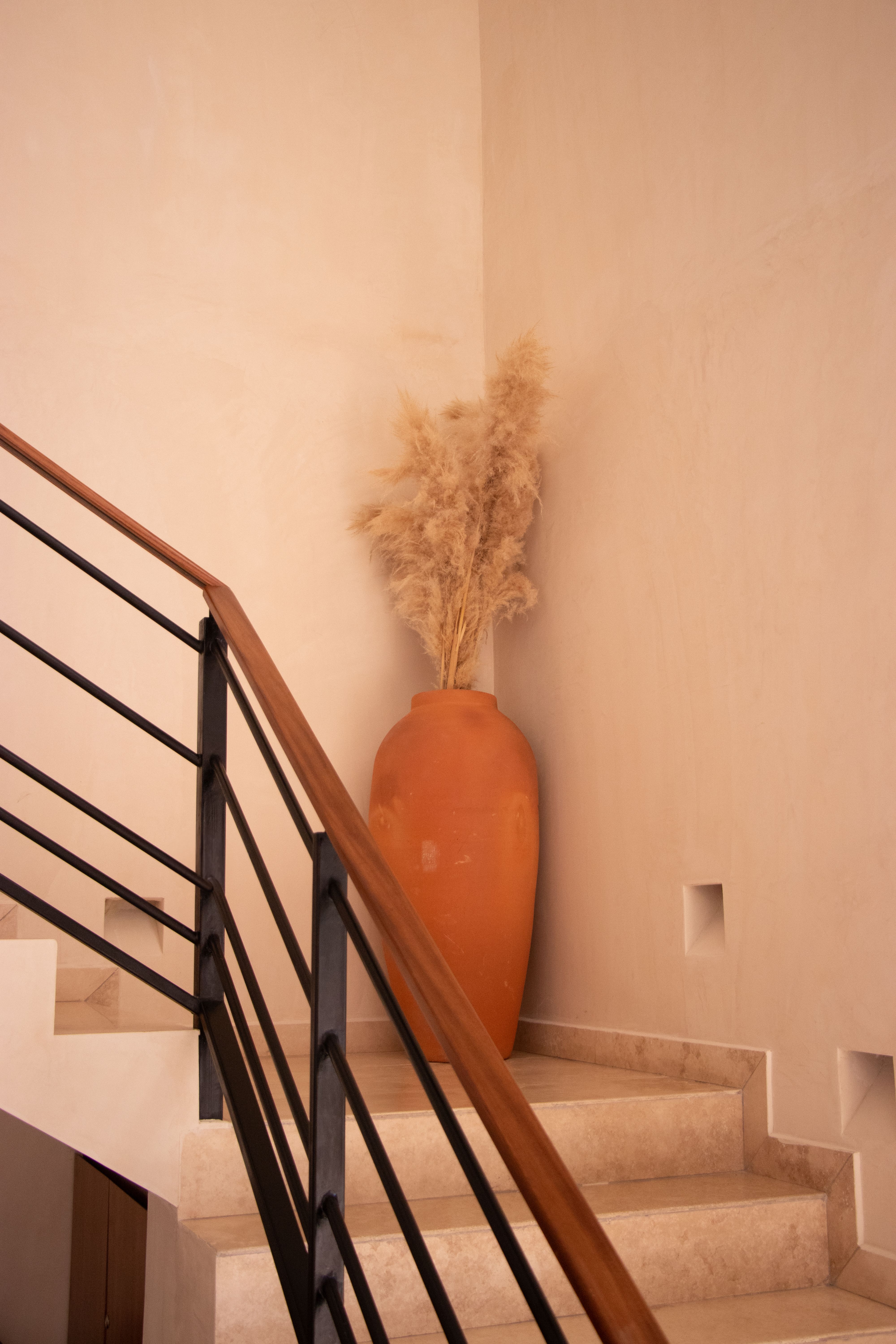Modern staircase with terracotta vase and pampas grass, showcasing minimalist interior design.