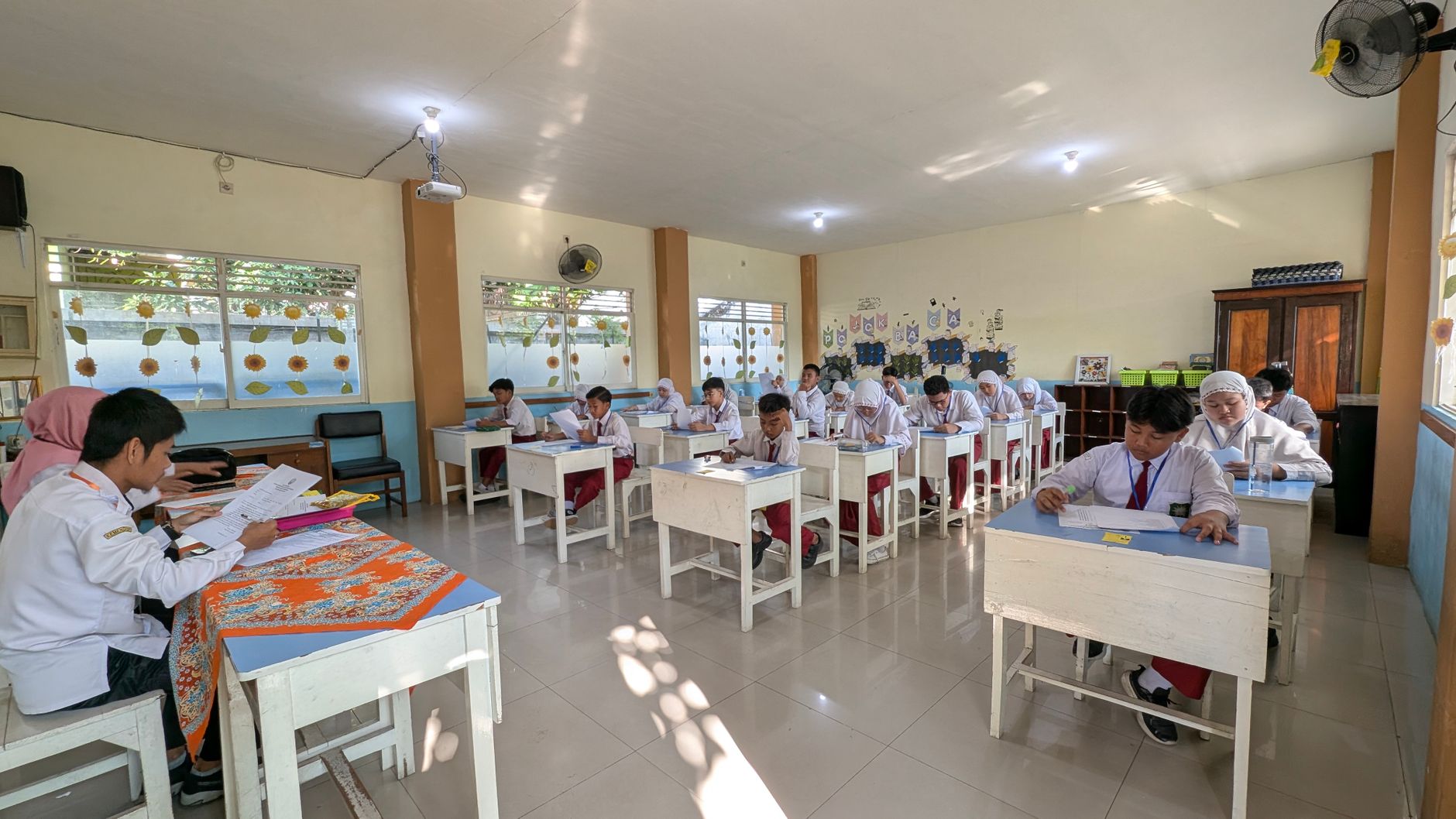 Students in an Indonesian classroom taking an exam under natural lighting.