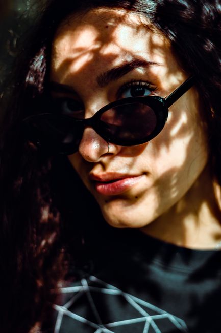 Young woman with sunglasses posing in shadows, exuding a mysterious and stylish vibe.