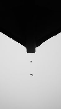 Minimalist black and white photo capturing raindrop from a roof edge, emphasizing zen simplicity.