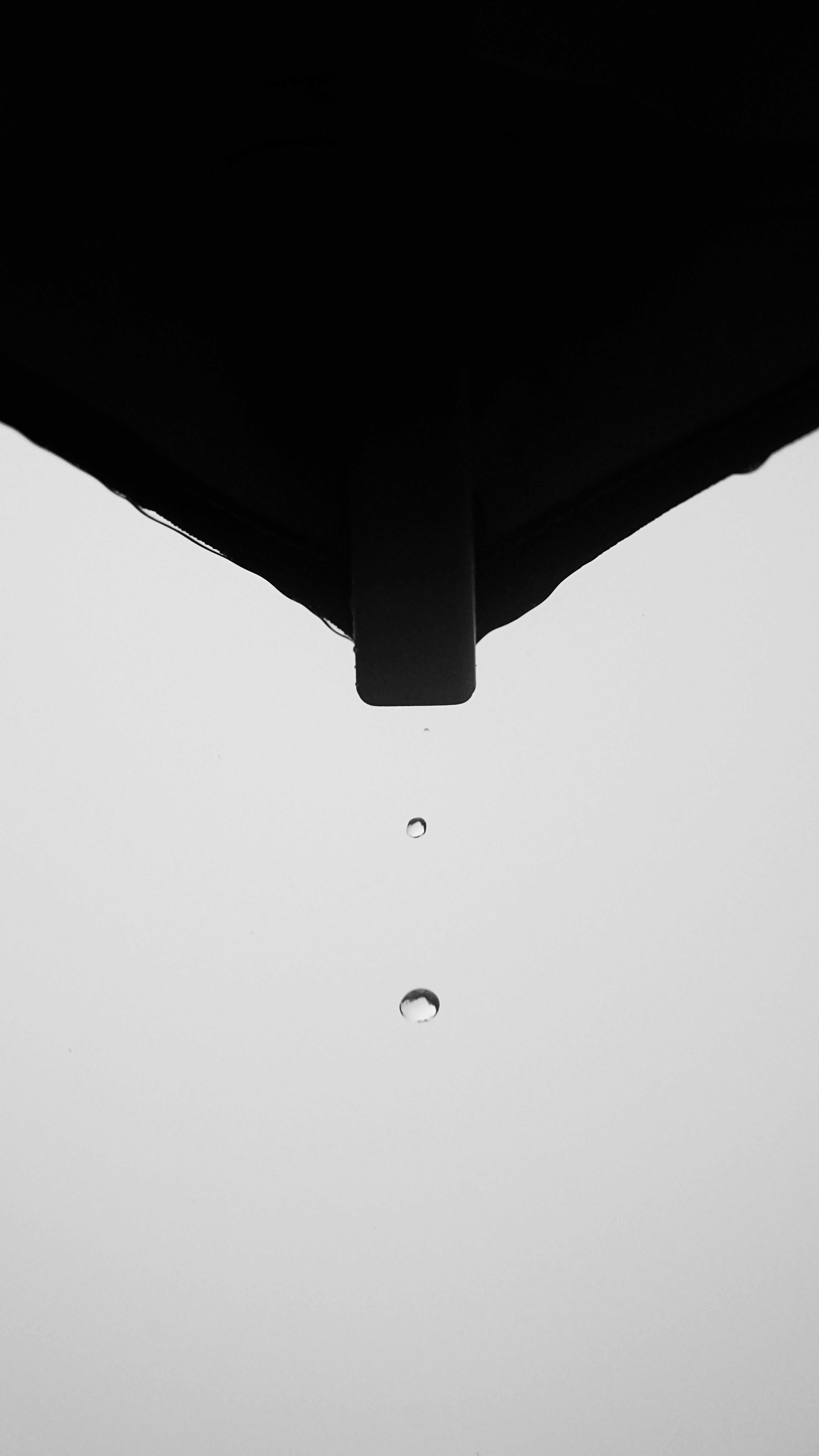 Ücretsiz Çatı kenarından düşen yağmur damlasını yakalayan, zen sadeliğini vurgulayan minimalist siyah beyaz fotoğraf. Stok Fotoğraflar