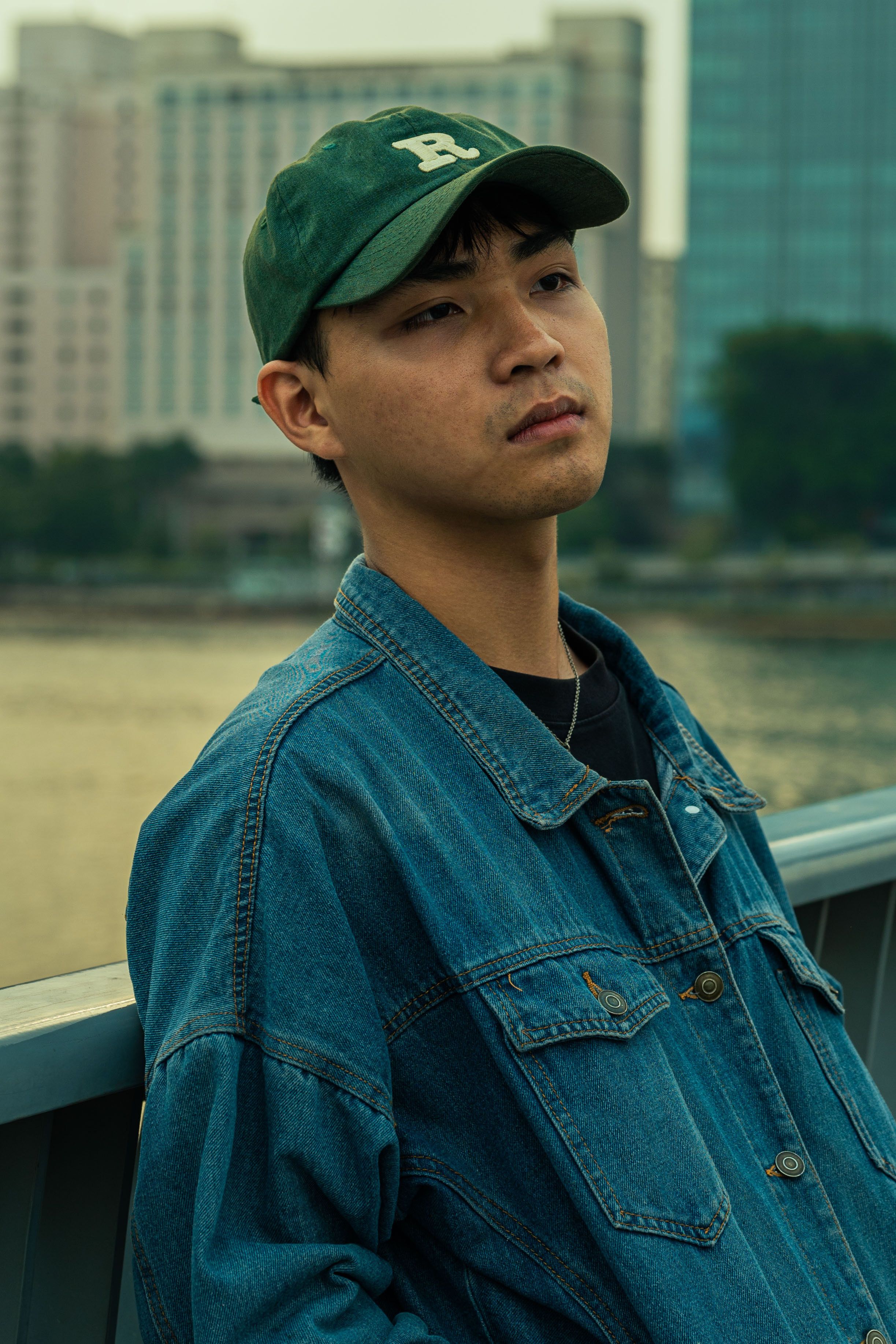 Casual young man in a denim jacket outdoors, urban landscape background.