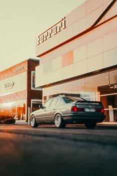 Classic dark car parked outside a Ferrari dealership during sunset, exuding vintage luxury vibes.