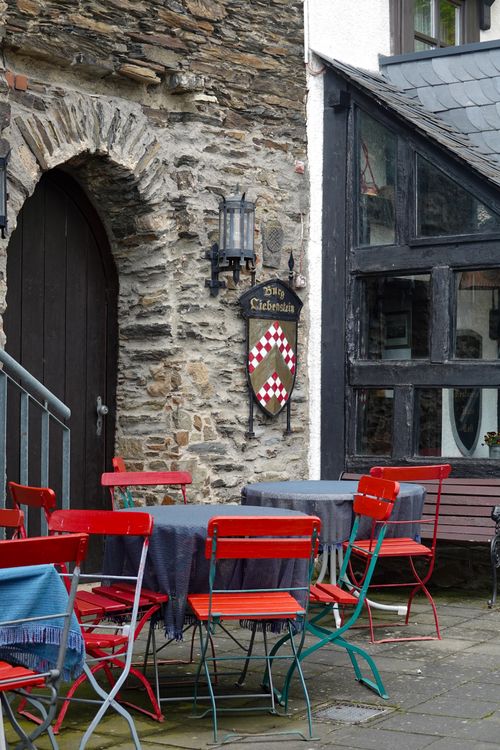 Free A picturesque outdoor cafe with red chairs and stone walls in a quaint village setting. Stock Photo