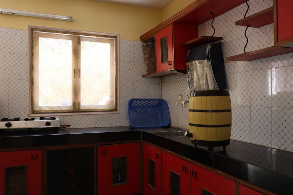 Bright Indian kitchen interior with red cabinets, gas stove, and window light.